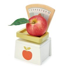 an apple sitting on top of a scale with a leaf sticking out of it's center