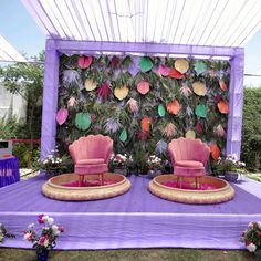 two pink chairs sitting on top of a purple table covered in paper flowers and greenery