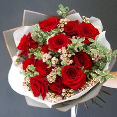 a bouquet of red roses and greenery in someone's hand on a gray background