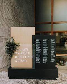 a book sitting on top of a black stand next to a plant in front of a building