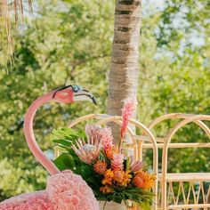 a pink flamingo sitting on top of a chair next to a flower vase filled with flowers