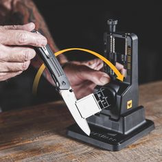 a man holding a knife on top of a wooden table next to a pair of scissors