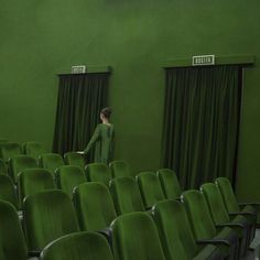 a woman standing in front of a green curtained room with rows of chairs around her