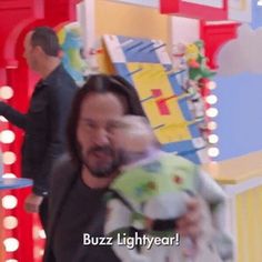 a man holding a stuffed animal in front of a carnival ride with lights on the sides