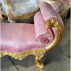 a pink and gold chaise lounge chair in a room with other chairs behind it