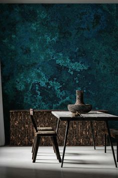 a table with two chairs and a vase on it in front of a green wall