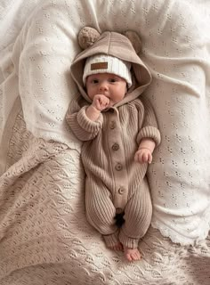 a baby laying on top of a bed wearing a knitted bear suit and hat