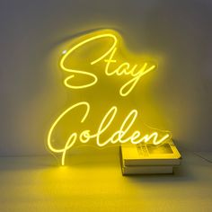 a yellow neon sign that says stay golden on top of a book in front of a white wall