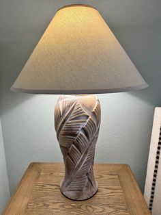 a lamp sitting on top of a wooden table next to a white vase with an intricate design