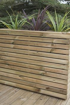 a wooden planter box on a deck with plants in the backgrounnd