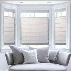 a white couch sitting under two windows in front of a window with roman shades on it