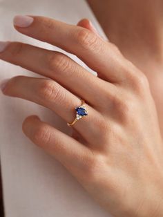 a woman's hand wearing a gold ring with a blue sapphire stone on it