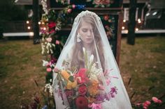 a woman wearing a veil and holding a bouquet in front of a decorated bench with candles