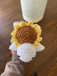 a person holding up a knitted sunflower on top of a white sheep's head