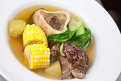 a white bowl filled with meat and vegetables on top of a table next to a fork