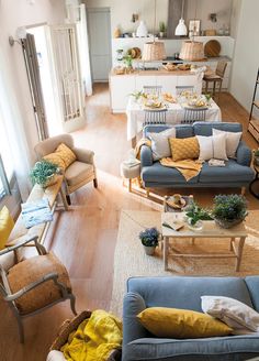 a living room filled with furniture next to a kitchen and dining room table covered in yellow pillows