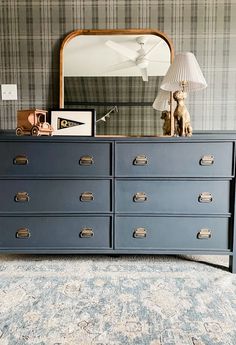 a dresser with many drawers in front of a mirror and lamp on top of it