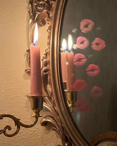 two candles are lit in front of a mirror with pink lipstick on the wall behind it