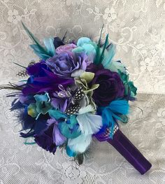 a bridal bouquet with purple, blue and green feathers on a white lace background