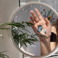 a woman holding her hand up in front of a mirror with a butterfly on it