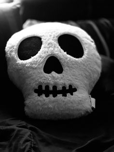 a white skull stuffed animal sitting on top of a bed next to a black pillow