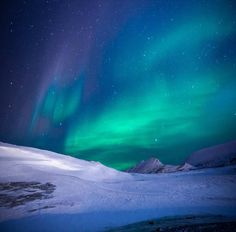 the aurora bore is shining brightly in the sky above snow covered hills and mountains,