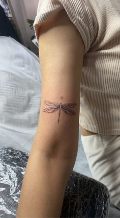 a woman's arm with a small dragonfly tattoo on the left side of her arm