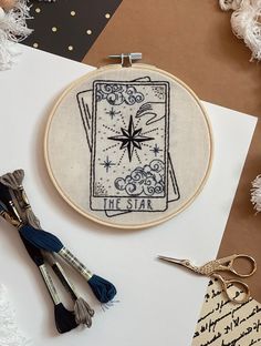 a cross - stitch pattern with scissors and thread on the table next to it is a star tarot card