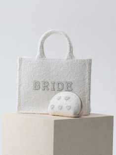 Show off your bridal style as you carry all your honeymoon essentials in Shiraleah's “Bride” Boucle Tote. Made from trendy white boucle fabric, this stylish and roomy tote features the word “Bride” embroidered in faux pearls and rhinestones. Take it with you on your bachelorette trip or anywhere you want to celebrate your big day. Pair with the matching “Bride” Boucle Ball Cap, or other items from Shiraleah's Hitched collection to complete your look! Shiraleah is a trend-driven lifestyle brand f Honeymoon Essentials, Spa Wraps, Bride Bag, Accessories Display, Bachelorette Trip, Zip Pouch, Framed Gifts, Pouch Bag, Belt Bag