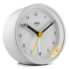 a white alarm clock with yellow hands and numbers on the face is illuminated by a light bulb