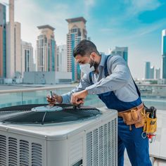 a man in blue overalls checking the air conditioner on top of a building