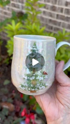 a hand holding a coffee cup with a christmas tree on the outside and snow on the inside