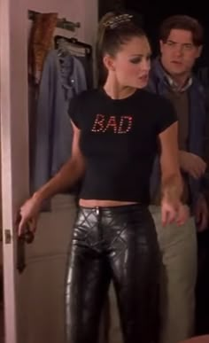 a woman standing in front of a mirror wearing black leather pants and a t - shirt with the word bad on it