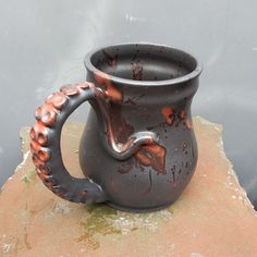 a black and orange vase sitting on top of a rock