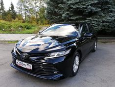 a black toyota camry parked in a parking lot next to some trees and bushes