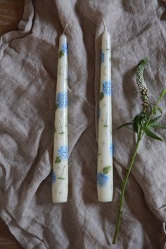 two candles sitting next to each other on top of a cloth covered table with flowers