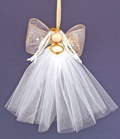 a white angel ornament hanging from a string on a purple background with gold accents