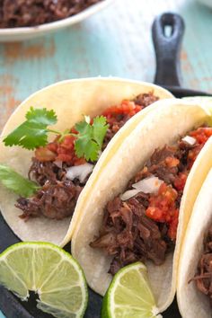 three tacos on a plate with lime wedges