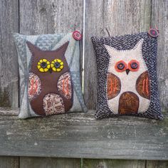 two decorative pillows sitting on top of a wooden bench next to each other and one has an owl design on it