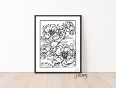 a black and white drawing of flowers in a frame on a wooden floor next to a wall