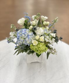 a vase filled with white and blue flowers on top of a marble tablecloth covered table