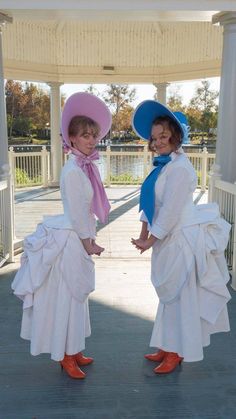 two women in white dresses and hats standing next to each other with their hands on their hips