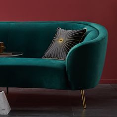 a green velvet sofa with gold accents and a black pillow on the end table next to it