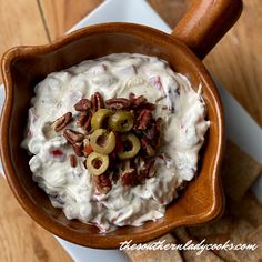 a wooden bowl filled with cream cheese and olives next to crackers on a white plate