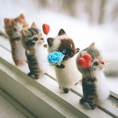 four little kittens are lined up on a window sill with fake flowers in their mouths