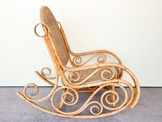 a wicker rocking chair sitting on top of a cement floor next to a white wall