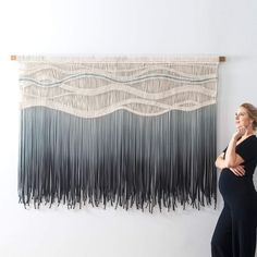 a woman standing in front of a wall hanging with black and white fringes on it