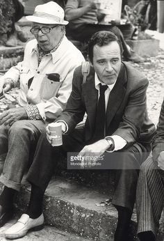 two men sitting on steps one holding a drink and the other looking at something in his hand