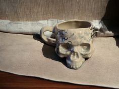 a ceramic skull shaped mug sitting on top of a cloth covered place mat next to a window