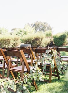 rows of wooden chairs lined up in the grass with greenery on each chair arm